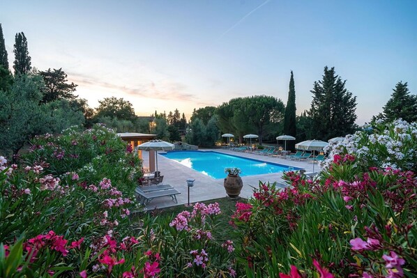 A swimming pool surrounded by lush greenery and flowers, with lounge chairs and umbrellas.