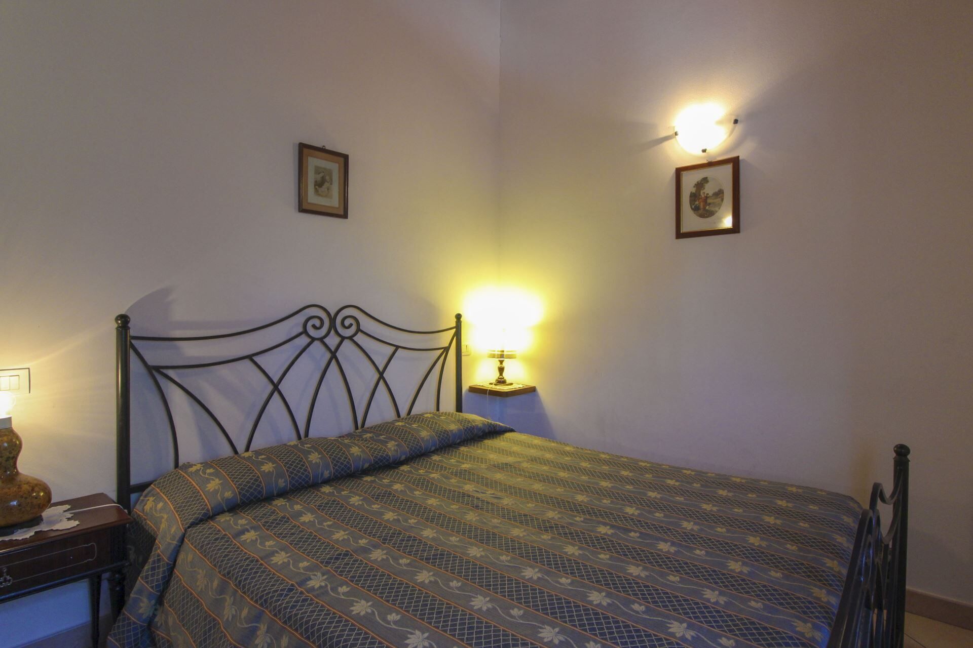 Un dormitorio con una cama, una mesita de noche, una lámpara y dos cuadros colgados en la pared.