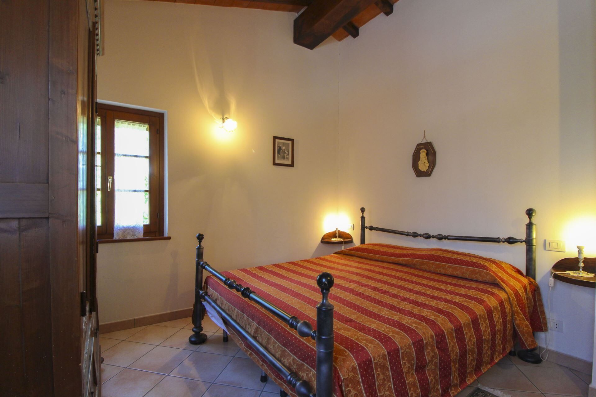 A bedroom with a bed, a window, a wall-mounted light, and a bedside table.