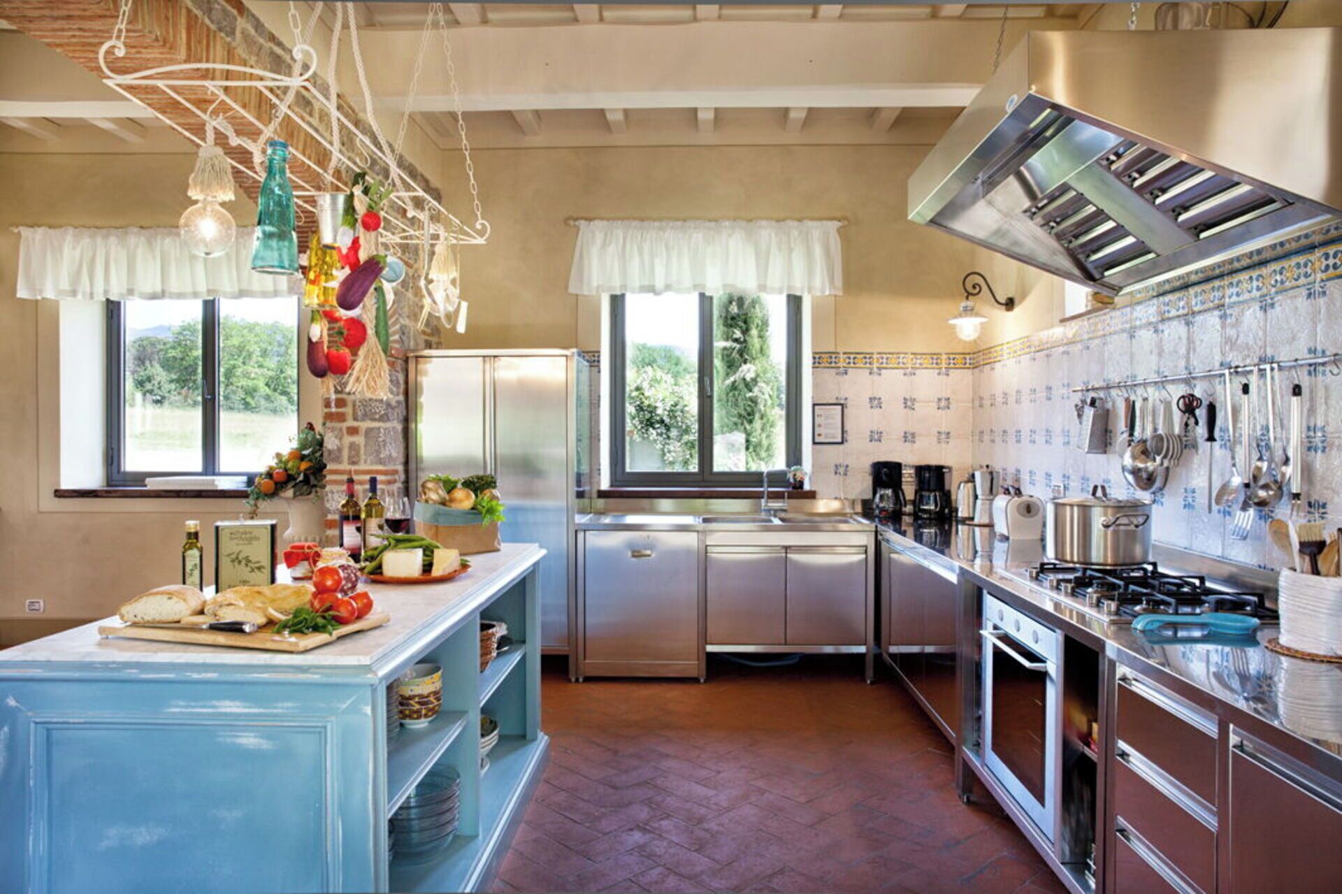 A kitchen with a blue island, stainless steel appliances, and a hanging light fixture.