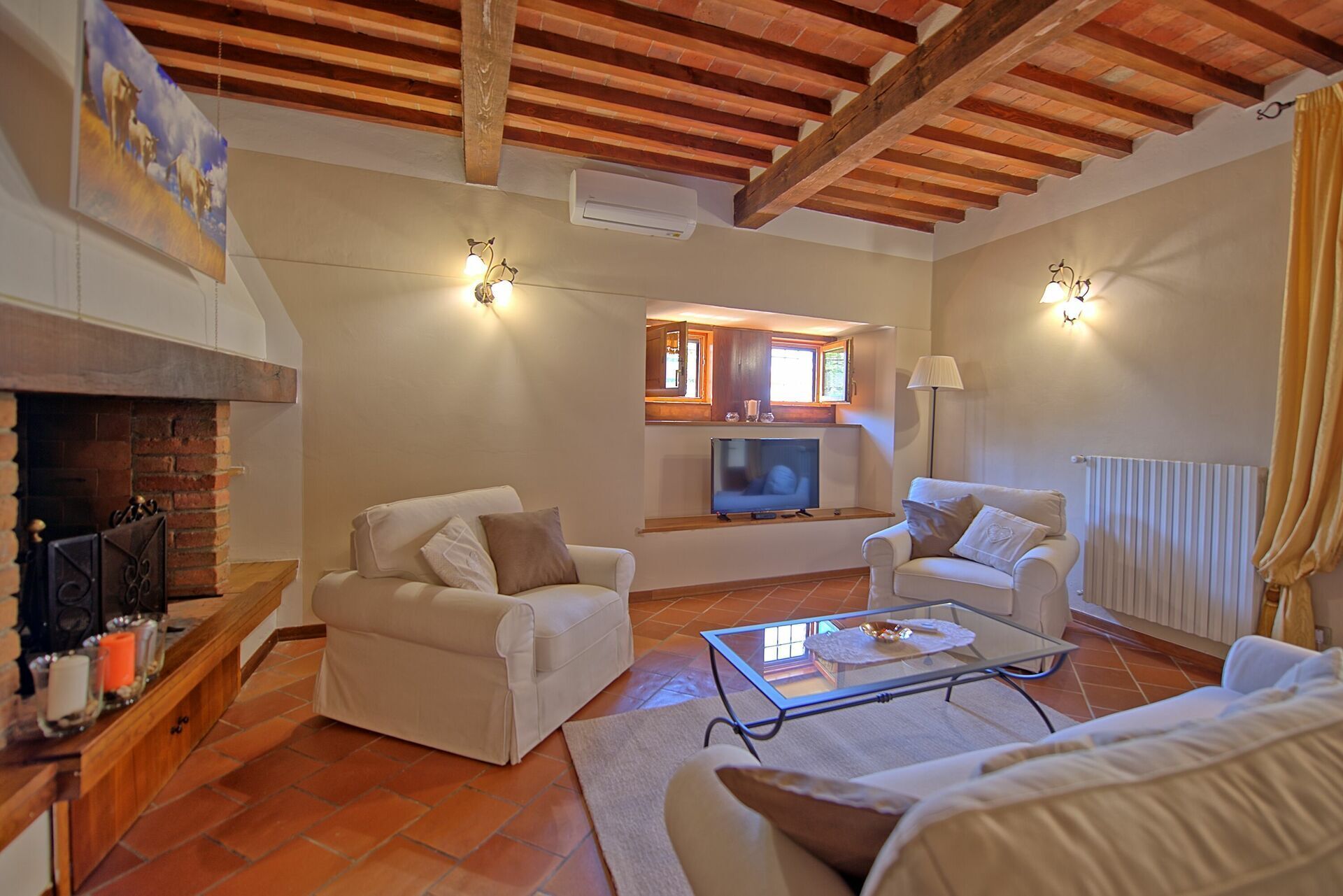 A living room with two white sofas, a glass coffee table, a fireplace, a TV, and a window with a view.