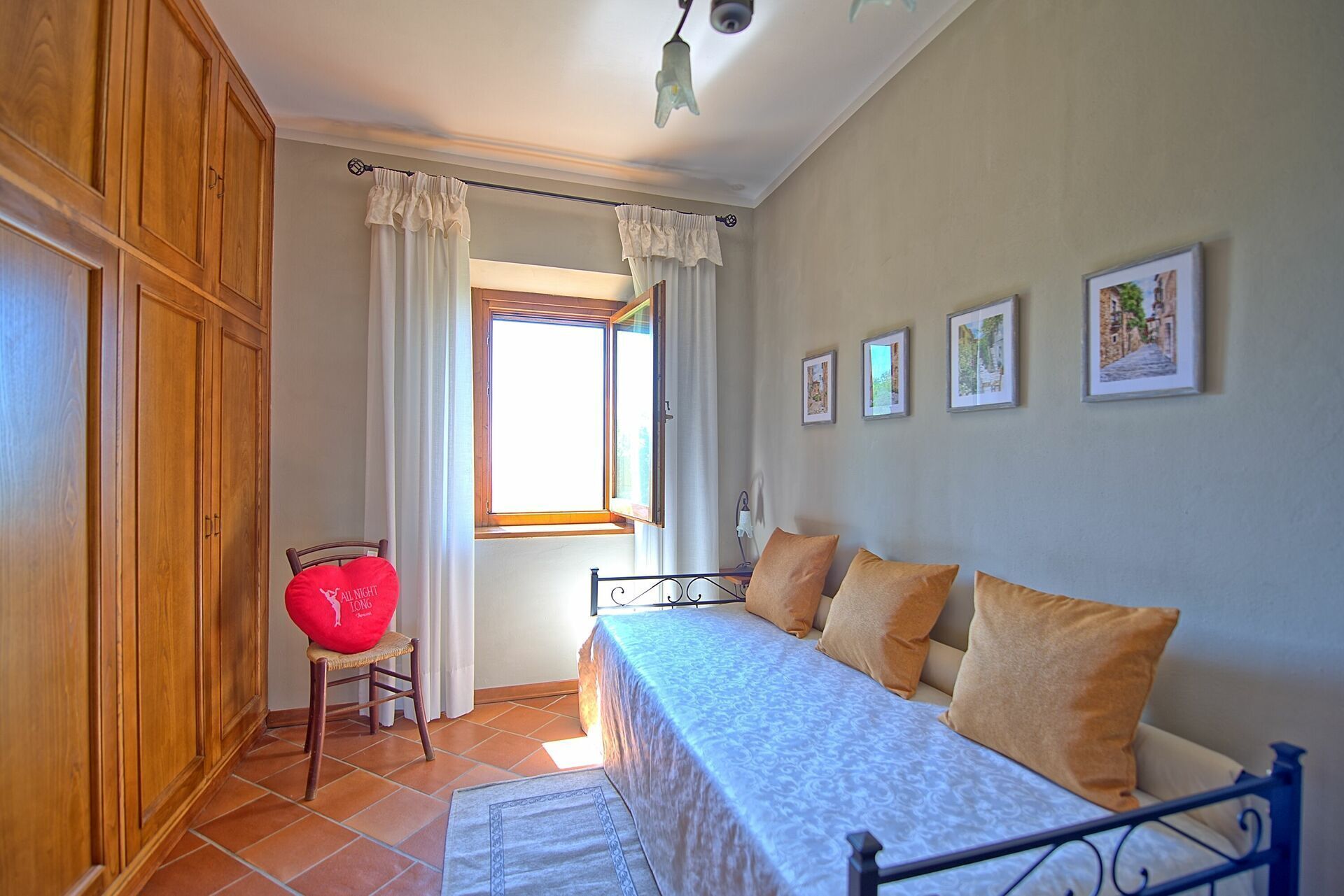 A bedroom with a bed, a chair, a wardrobe, and a window with curtains.