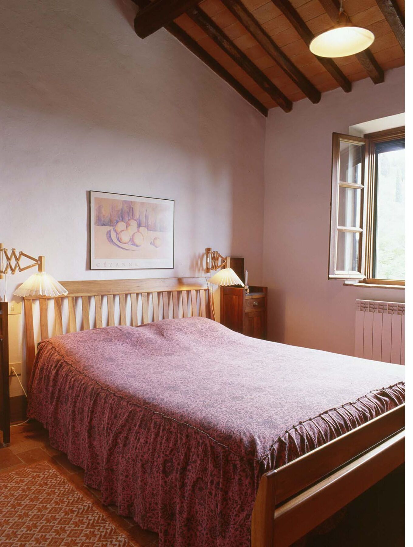 Une chambre à coucher avec un lit en bois, un radiateur, une fenêtre donnant sur un beau paysage et un tableau accroché au mur.