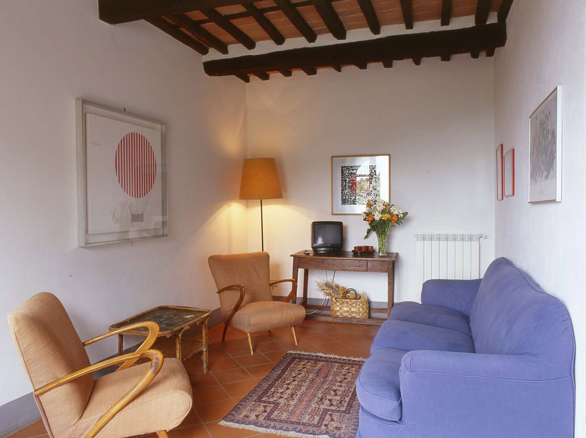 Ein Wohnzimmer mit einem blauen Sofa, zwei Sesseln, einem kleinen Tisch, einer Lampe, einem Fernseher und einer Heizung.