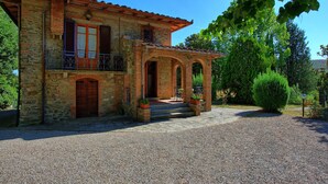 Un edificio in pietra con tetto a tegole, un balcone e un vialetto sterrato.