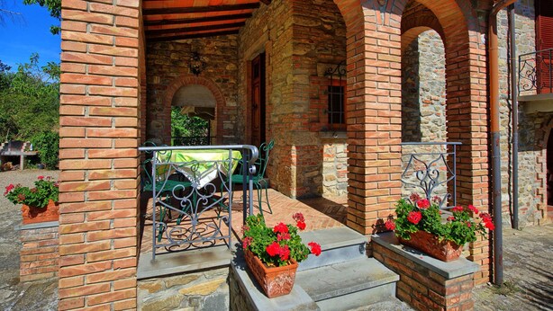 Un edificio in mattoni con un patio coperto, che include una panchina in metallo e piante in vaso.
