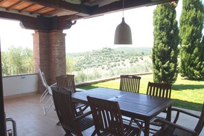 A covered patio with a wooden table and chairs, a hanging pendant light, and a view of a hilly landscape. - Beautiful apartment for 6 guests with WIFI, TV, patio and panoramic view (Follonica)