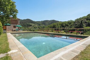 A rectangular outdoor swimming pool with a stone border, surrounded by a wooden deck and picnic tables.