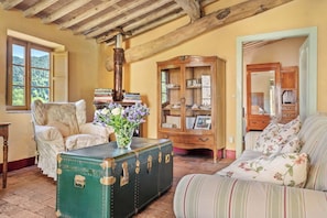 A room with a green trunk, a floral sofa, a wooden cabinet, and a window with a view of trees.