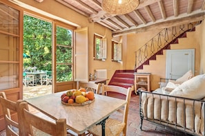 A dining area with a table set for two, a wicker basket of fruit, and a staircase leading to a bedroom.