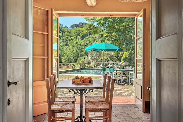 An open door leading to a patio with a table, chairs, and a green umbrella.