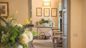 Un corridoio con pavimento in legno, un tavolo metallico con cesti, una sedia e una parete decorata con stampe botaniche incorniciate.