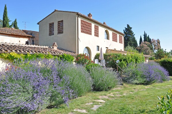 Un edificio tradicional con tejado de tejas, un jardín con lavanda y un cielo azul despejado.