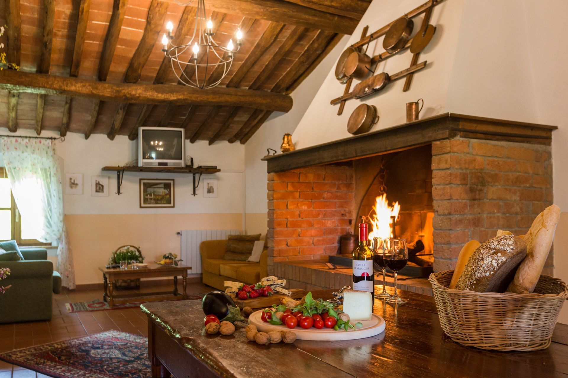 A cozy living room with a fireplace, wooden beams, a television, and a table with food and drinks.