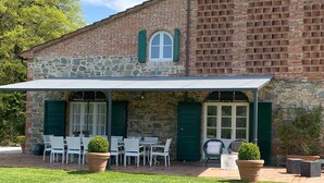 A stone building with a covered patio area featuring white chairs and tables, green shutters, and potted plants. - Stunning private villa for 12 people with A/C, WIFI, private pool, TV and panoramic view (Orentano)