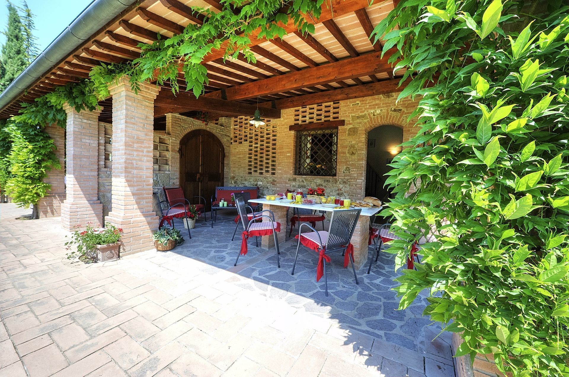 An outdoor patio with a stone floor, a wooden pergola, and a brick wall.