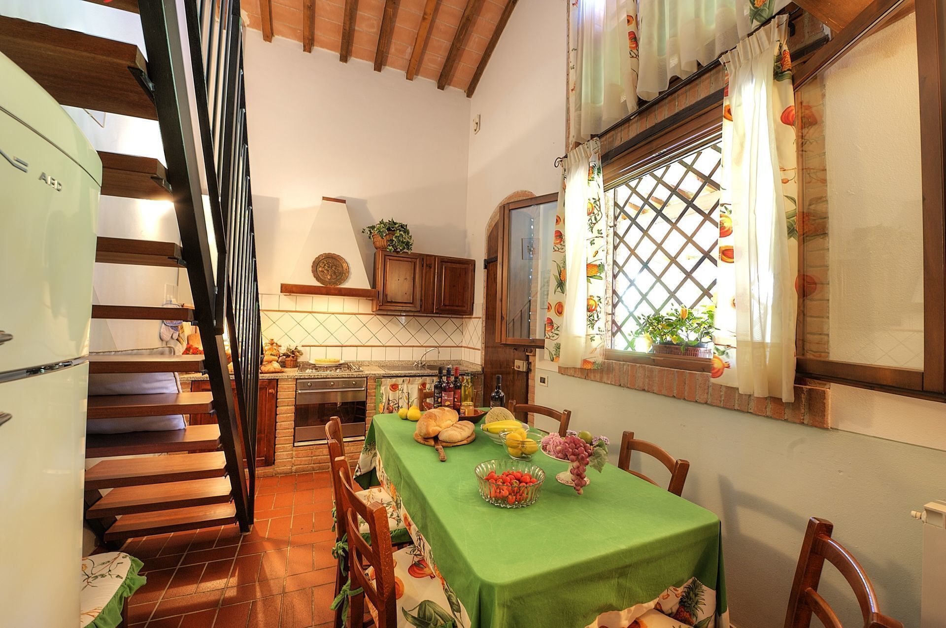 A kitchen with a dining table set for a meal, wooden cabinets, a stove, and a window with curtains.