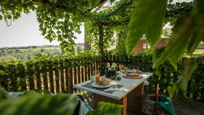 Une table dressée à l’extérieur, avec vue sur un vignoble, entourée de verdure et d’une clôture en bois.