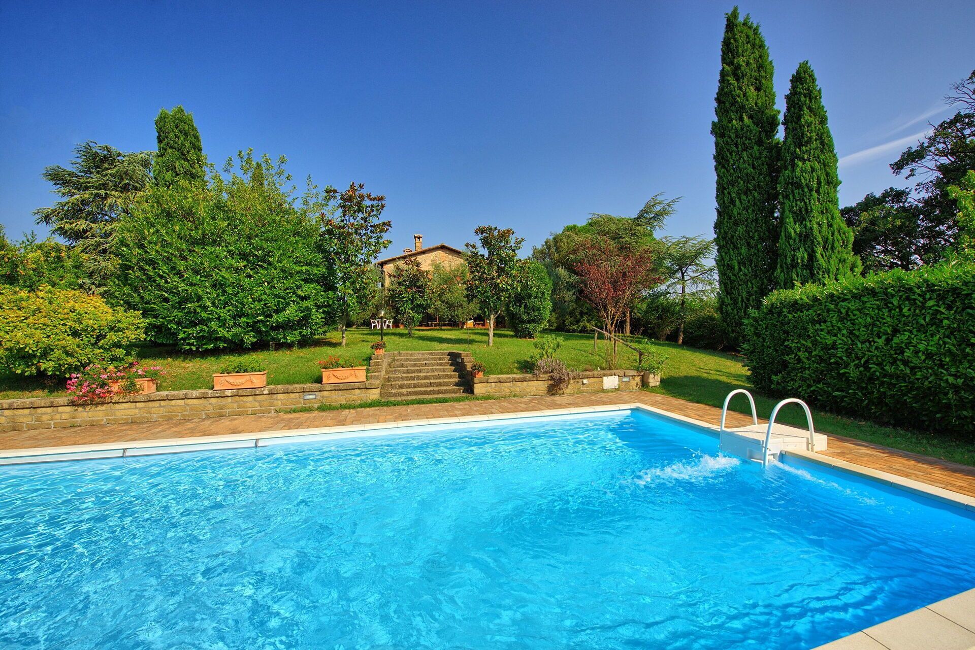 Une piscine rectangulaire à l’eau d’un bleu limpide, entourée d’une terrasse en briques.