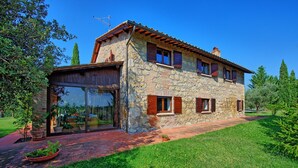 A stone house with a large glass door, a wooden balcony, and a well-maintained garden. - Beautiful private villa for 7 guests with private pool, A/C, TV and panoramic view (Cetona)