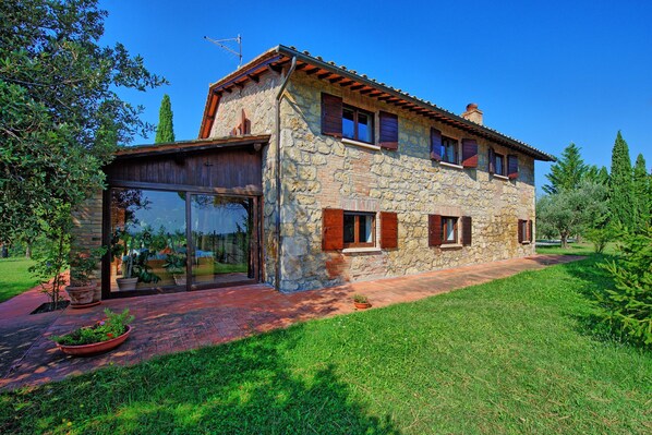 Una casa de piedra con un gran ventanal, un balcón de madera y un jardín bien cuidado.