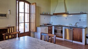 Une cuisine dotée d’un plan de travail en marbre, de meubles en bois, d’un four encastré et d’une fenêtre avec un cadre en bois.