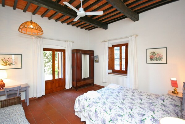 A bedroom with a bed, a desk, a chair, a ceiling fan, and a window with curtains.