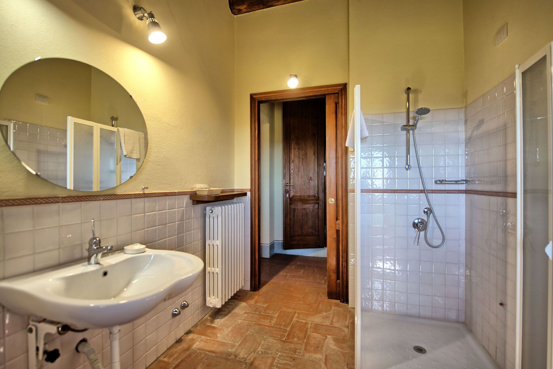 Une salle de bain équipée d’un lavabo, d’un miroir, d’une douche et d’une porte donnant sur une autre pièce.