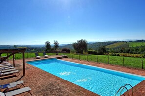 A rectangular swimming pool with a clear blue water surface, surrounded by a brick patio with lounge chairs.