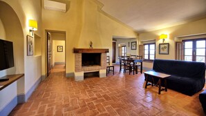 Amplia sala de estar con chimenea, una mesa de comedor con sillas, un sofá y un televisor montado en la pared.