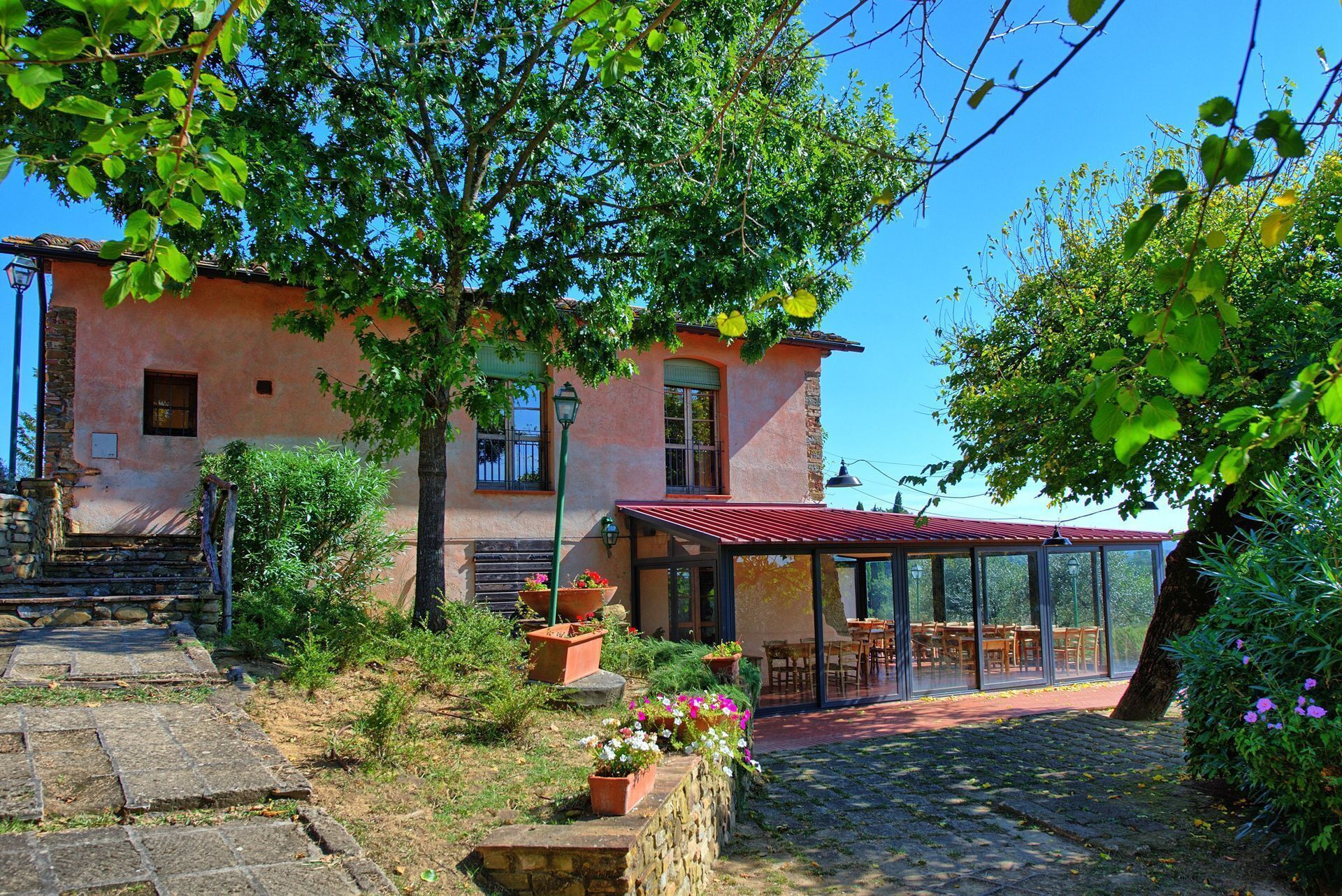 Ein rustikales Gebäude mit einer Steintreppe, die zu einer Holztür führt, umgeben von üppigem Grün und einem patioartigen Glasbereich.