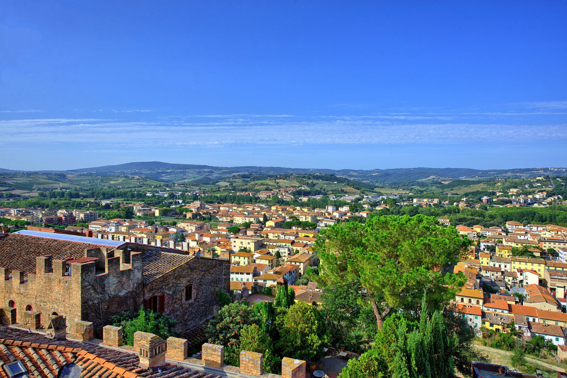 A historic town with a prominent stone building in the foreground, surrounded by a densely packed residential area with terracotta roofs.
