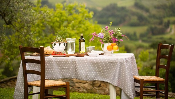 A table set outdoors with a view of rolling hills, a white polka dot tablecloth, and various food items and drinks.