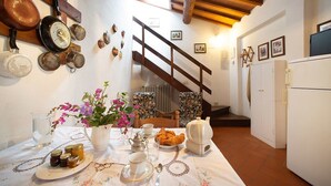 A kitchen with a dining table set for breakfast, featuring a variety of dishes, a pitcher of flowers, and a rustic wooden staircase.