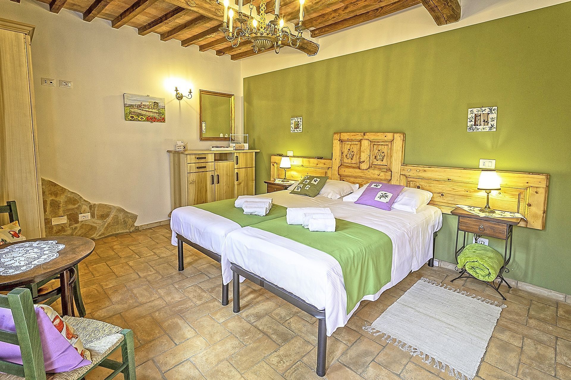 Una camera da letto con un letto matrimoniale, una testiera in legno, lampade sui comodini, un tavolino con una sedia e una parete verde.