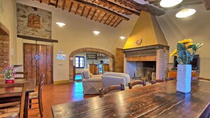 Um interior rústico com área de jantar, lareira e cozinha visíveis por um arco.
