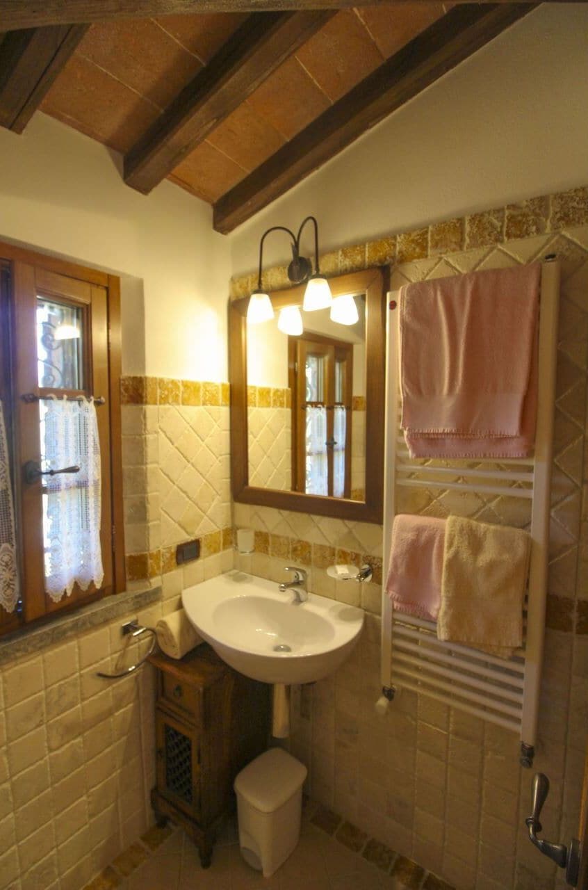 Une salle de bain avec un lavabo blanc, un miroir, un porte-serviettes avec des serviettes roses et un meuble en bois.