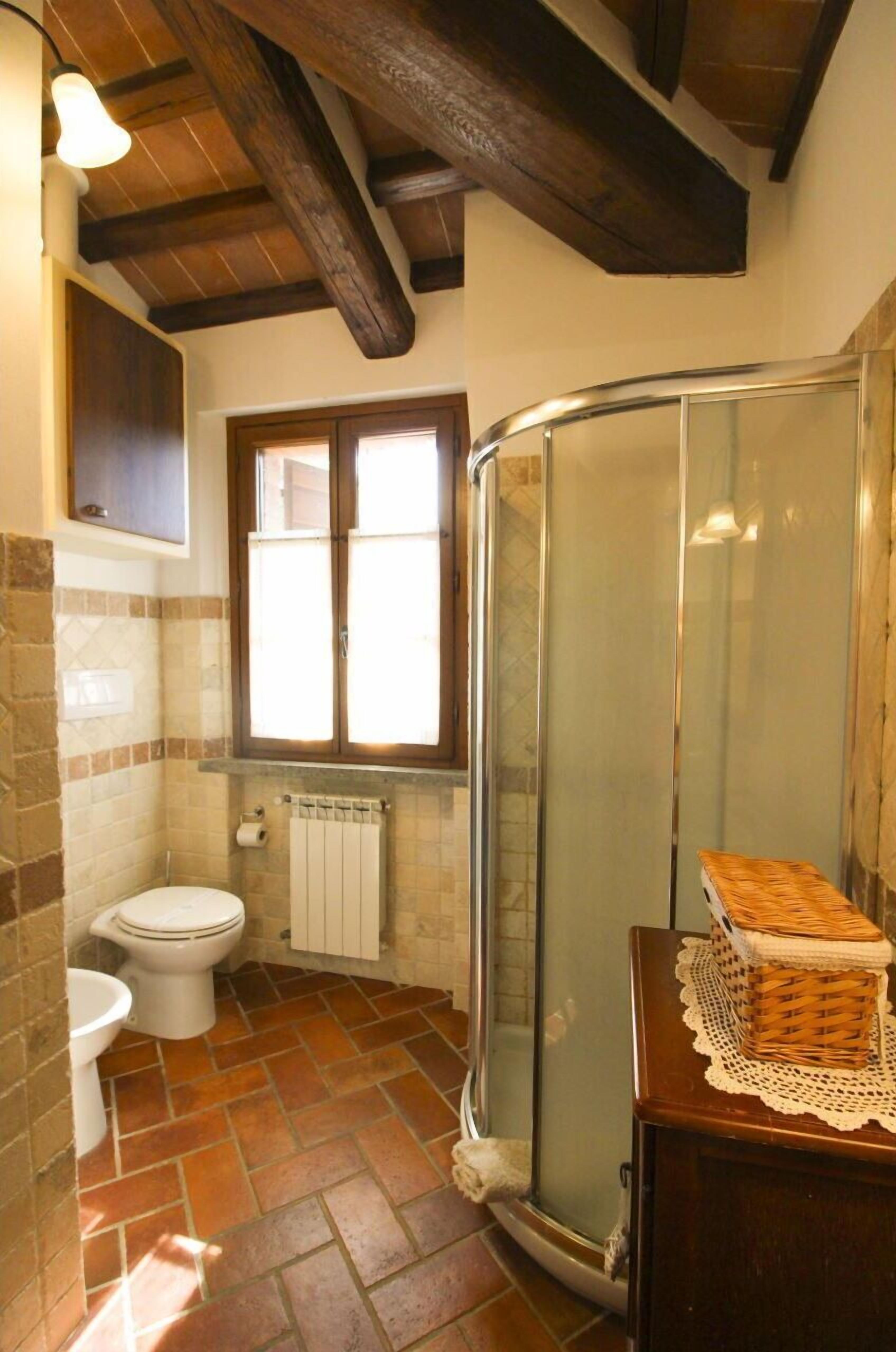 A bathroom with a shower, a toilet, a radiator, and a window.