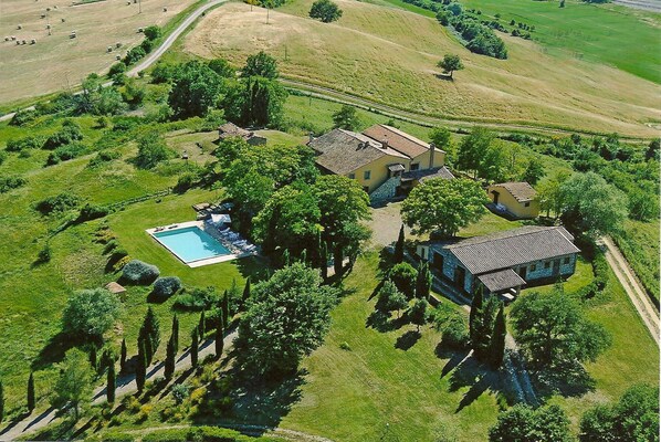 Vista aérea de una propiedad con piscina, varias edificaciones y follaje circundante.