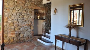 A room with a stone wall, a wooden staircase, a table with a vase, and a mirror on the wall. - Lovely apartment for 6 guests with pool, WIFI, TV, patio, pets allowed and panoramic view (Centeno)
