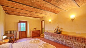 Un dormitorio con pared de piedra, cómoda de madera, cama con ropa blanca y radiador.