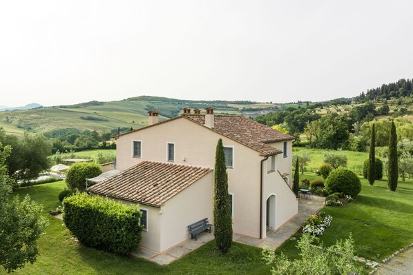 A two-story house with a tiled roof, surrounded by well-maintained gardens and a scenic countryside view.