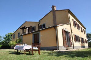 Ein zweistöckiges Haus mit Balkon, einem Tisch für Mahlzeiten im Freien und einem Rasen.