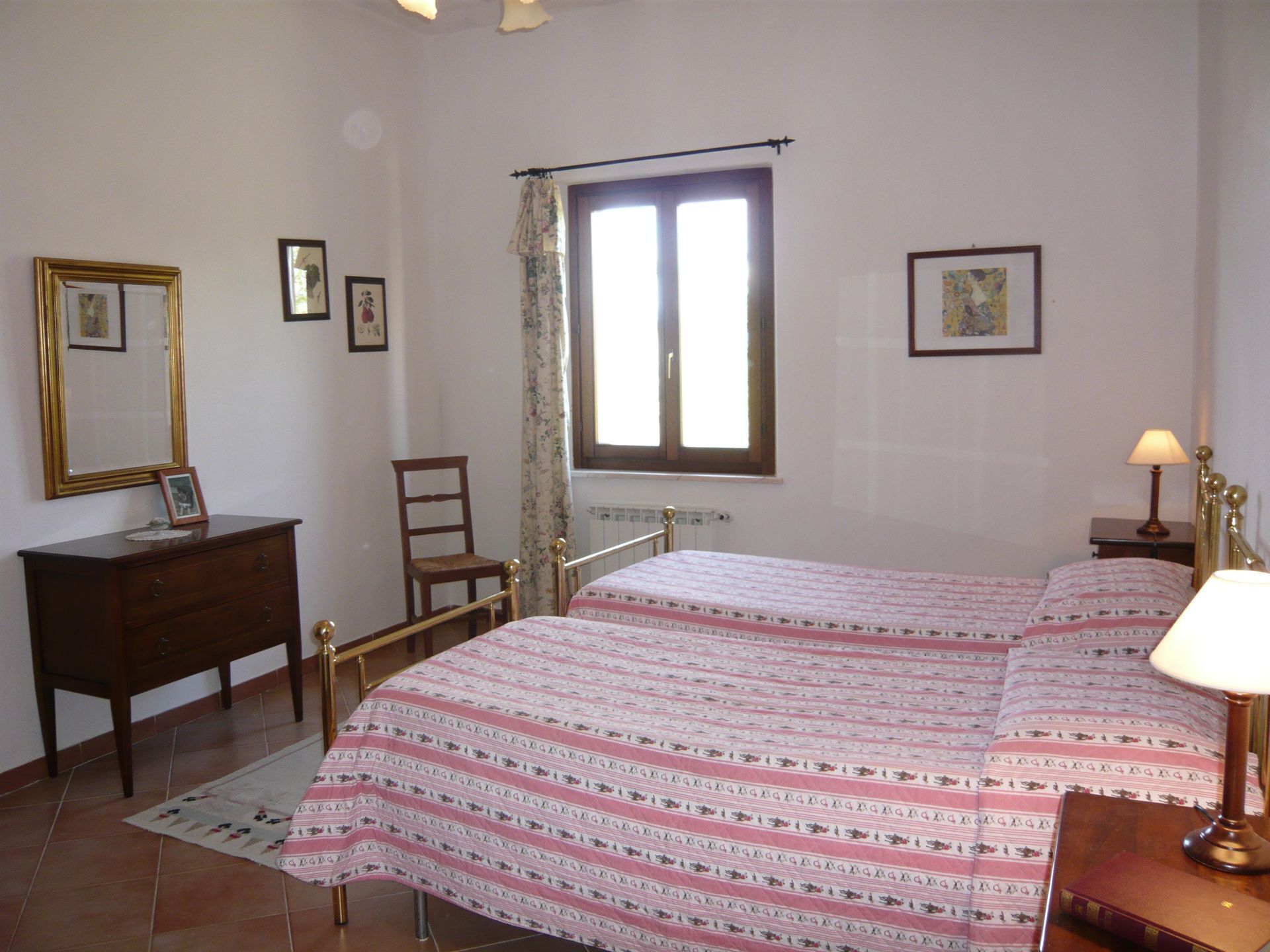 A bedroom with a bed, a dresser, a chair, a window with curtains, and a lamp.