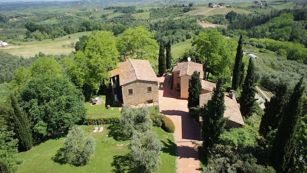 Une maison en pierre, avec un toit de tuiles, entourée d’une végétation luxuriante et de collines ondulantes.