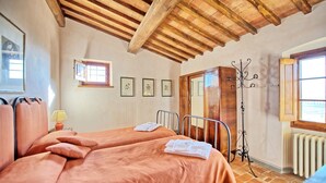 Ein Zimmer mit zwei Betten, Holzbalkendecke, Heizkörper und gerahmten Bildern an der Wand.