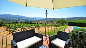Eine Terrasse mit Korbmöbeln, einem Pool und Blick auf ein Weinberg.