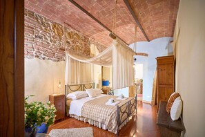 A bedroom with a canopy bed, a brick wall, wooden flooring, and a wooden wardrobe.