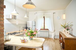 A modern kitchen with a central island, stainless steel appliances, pendant lighting, and a view of the outdoors through a window with curtains. - Wonderful  villa for 8 people with private pool, WIFI, TV and panoramic view, close to Montepulc... (Bagno Vignoni)