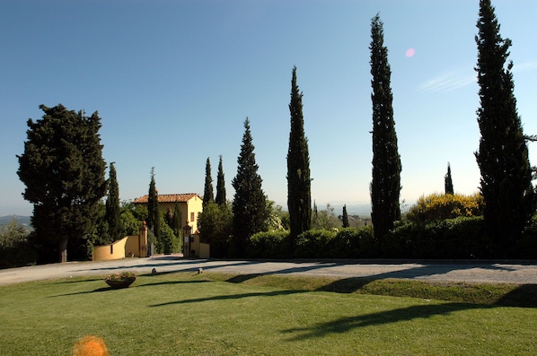 A landscaped garden with a building, tall cypress trees, and a clear sky.
